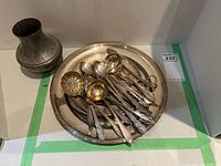 Photo showing round metal serving tray with assorted spoons and ladles inside.