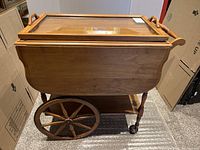 Full side view of the wooden tea cart showing large spoked wheels and carved floral details on panel.