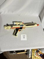 Front full view of off-white Star Wars Clone Trooper toy blaster with orange trigger and barrel tip, featuring scope and decals, showing some wear.