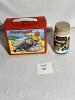 Red Rough Rider plastic lunch box with white handle alongside Six Million Dollar Man thermos showing box front