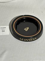 Top-down photo of black ceramic Guinness advertising coin tray with gold harp logo and GUINNESS text on rim.