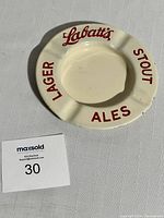 Cream-colored metal enamel ashtray with red Labatt's Lager Ales Stout lettering, showing used condition.