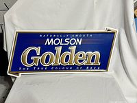 Full view of large Molson Golden beer sign with bold embossed lettering on blue background