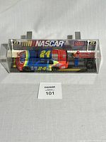 Side view of clear plastic display case holding the colorful NASCAR race car with number 24 and Mega Bloks logos.