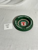 Green metal ashtray with Tennent's Pilsner branding on white background.