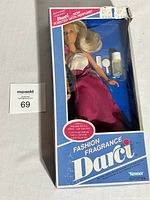 Front view of unopened box containing the 1980 Kenner Fashion Fragrance Darci doll, showing the doll dressed in magenta skirt and white top with accessories inside.