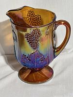 Front view showing grape cluster and leaf relief detail with iridescent amber carnival glass finish and pedestal base.