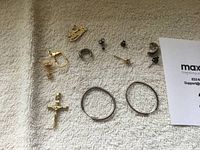 Lot showing various 14k to 16k gold jewelry pieces including earrings, a pendant, rings, and small studs on a white textured fabric.