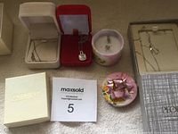 Overview photo showing two jewelry boxes with silver chains, a round floral container holding earrings, and a decorative box with a pink bow.