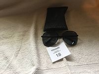 Black aviator sunglasses positioned on a black Quay Australia branded pouch case on a beige fabric surface.