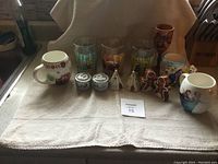 Overall view of all items on a white towel showing cups, mugs, shakers, wooden goblet and gingerbread figurines.