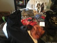 Blurry photo of multiple costumes and accessories on table including robes and red costume pieces.