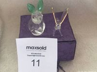 Photo showing both crystal figurines placed on a purple box on carpeted floor, with auction number card in front