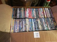 Photo showing two rows of assorted DVD movies in plastic cases inside a cardboard box, covers and spines visible.