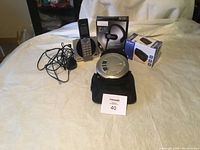 Panasonic MP3 player with control buttons and carrying case, VTech cordless phone with charger, Sound Blast Sport BLAST earbuds in box, and Start clock radio in box arranged on bed.