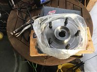 New rear wheel hub assembly on wooden surface with plastic wrapping, showing bolt studs and bearing flange surface.