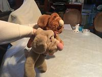 Side angled view of two dog hand puppets held up, showing plush texture and facial details.