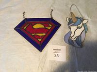 Both light catchers, Superman symbol and unicorn design on a beige cloth background with MaxSold lot card