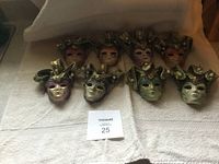 Eight assorted mini ceramic hanging masks arranged on a towel. Various colors and decorative beaded headpieces.
