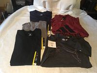 Five men's size large T-shirts laid out on a white surface, showing front designs and tags.