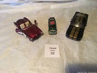 Photo showing three solid metal model collector cars: red convertible, green race car, black coupe with gold stripes.
