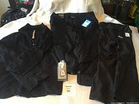 Three black women's tops laid out on a flat surface, showing a button-up shirt, zip-front top, and another button-up shirt, with a small packaged item (possibly a key or accessory) in front.