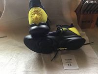 Side view of sneakers showing black and yellow color scheme and lion's head emblem on heel