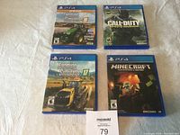 Four PS4 game cases and discs placed on white fabric background. Titles include Farming Simulator 19, Call of Duty Infinite Warfare, Farming Simulator 17, and Minecraft PlayStation 4 Edition.