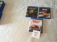 Three PS4 game cases on a white surface showing Minecraft, Need for Speed Heat, and Need for Speed Payback game covers.