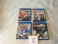 Four PS4 game cases closed on a fabric surface with visible covers for Cars 3 Driven to Win, LEGO Harry Potter Collection, Sonic Forces, and LEGO Batman 3 Beyond Gotham.