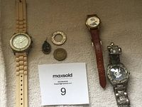 Three wristwatches and three coins/medallions laid on fabric surface with MaxSold tag
