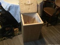 Front view of large square wicker hamper with open lid showing fabric lining and some Christmas decorations inside.