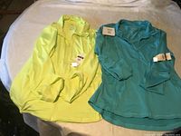 Photo shows two new women's long-sleeve shirts in lime yellow and teal blue laid flat on a surface, size large with tags attached.