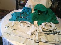 Four hooded sweatshirts on a white surface, two teal/green and two light gray.