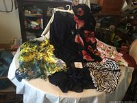 Assorted woman's clothing displayed on a table, various floral patterns, black, yellow-green, and zebra print items visible.