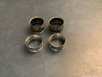 Top view of all four napkin holders showing two different styles: two with ornate floral and scroll designs and two with simpler engraved patterns.