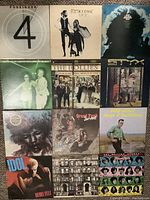 12 vinyl LP records arranged flat in a 4 by 3 grid showing cover artwork for Foreigner, Fleetwood Mac, Hendrix, The Hollies, and others.