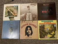 Photo showing six LP album covers including Eagles, Solomon Burke, Buffalo Springfield, The Byrds, David Bromberg, and Jackson Browne arranged side by side on carpeted floor.
