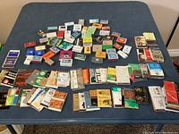 Overview photo showing a large assortment of empty matchbooks and matchboxes spread out on a blue surface.