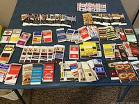 Full view of assorted empty matchbooks and matchboxes laid out on a table from a top perspective.
