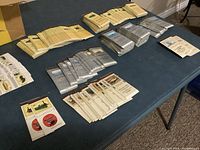 Overhead view of multiple stacks of matchbooks and matchboxes on a table, showing the variety of designs including ships and cars.
