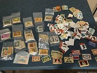 Photo showing multiple stacks of vintage matchbox labels sorted in small clear plastic bags and loose stacks on a flat surface.