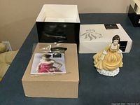 Photo showing the Royal Doulton Coralie figurine standing next to the original box and informational card on a flat surface.