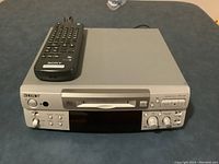Front view of silver Sony MiniDisc deck with front-loading disc tray, control knobs, display, remote resting on top