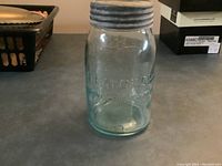 Clear glass preserving jar standing upright on a flat surface, showing overall shape and lid.