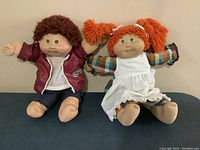 Photo of two dolls seated side by side showing full bodies and outfits.