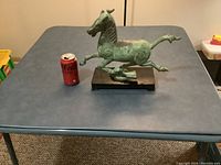 Front view of verdigris metal horse sculpture standing on bird figure, soda can for scale