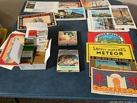 Full assortment of vintage empty matchbooks and matchboxes displayed on a table, showing various labels and boxed sets.