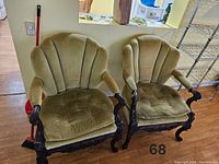 Two vintage green velvet upholstered armchairs with carved dark wood frames, placed side by side on a hardwood floor.