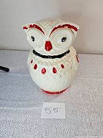 Front view of vintage owl-shaped bisque cookie jar with red, black, and white paint.